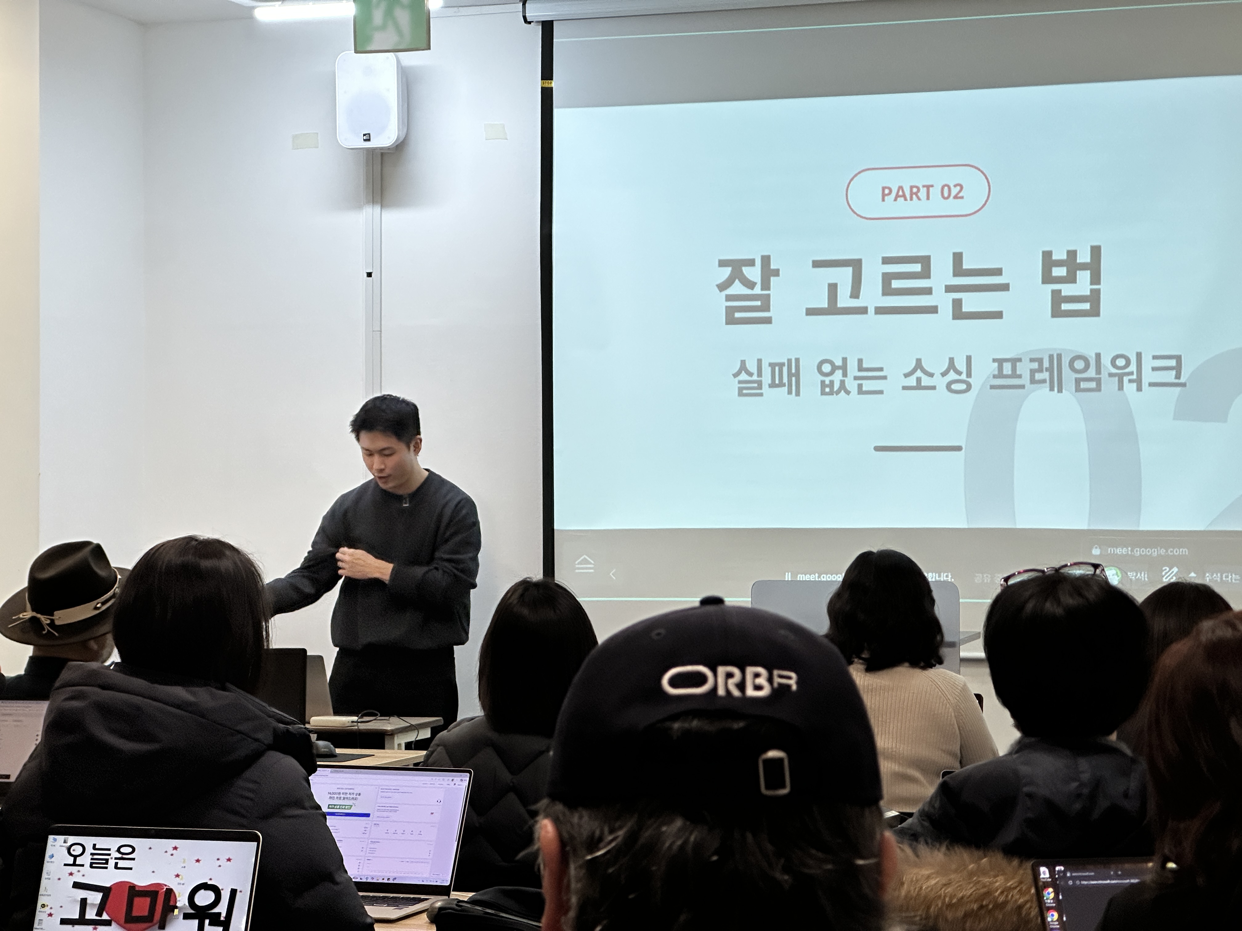 인베이더스쿨 셀러 강의 현장 사진. 1인 셀러들이 강의를 듣고 있고 화면에는 소싱 프레임워크 강의 자료가 보입니다.